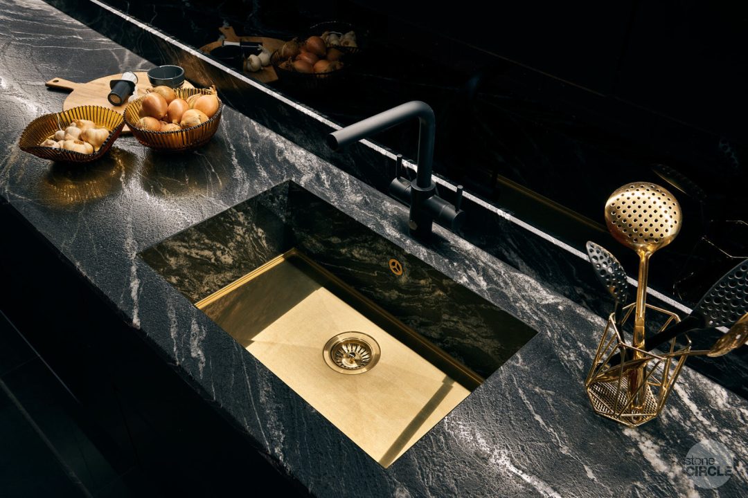 black quartz stone kitchen countertop with a gold kitchen sink embedded in the stone